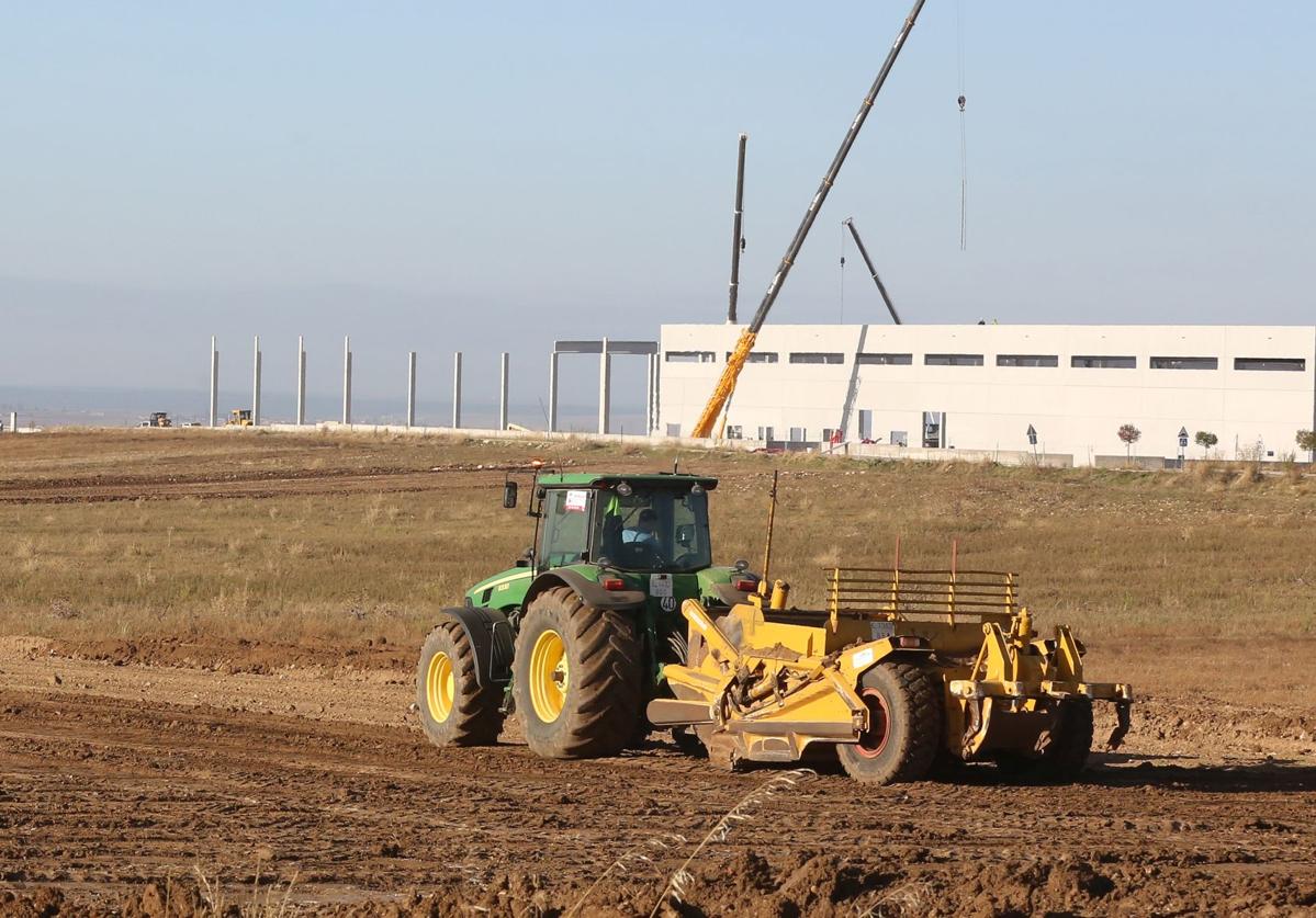 Un tractor trabaja en los terrenos de la urbanización del polígono de Los Hitales, y al fondo las obras de la planta de Drylock.