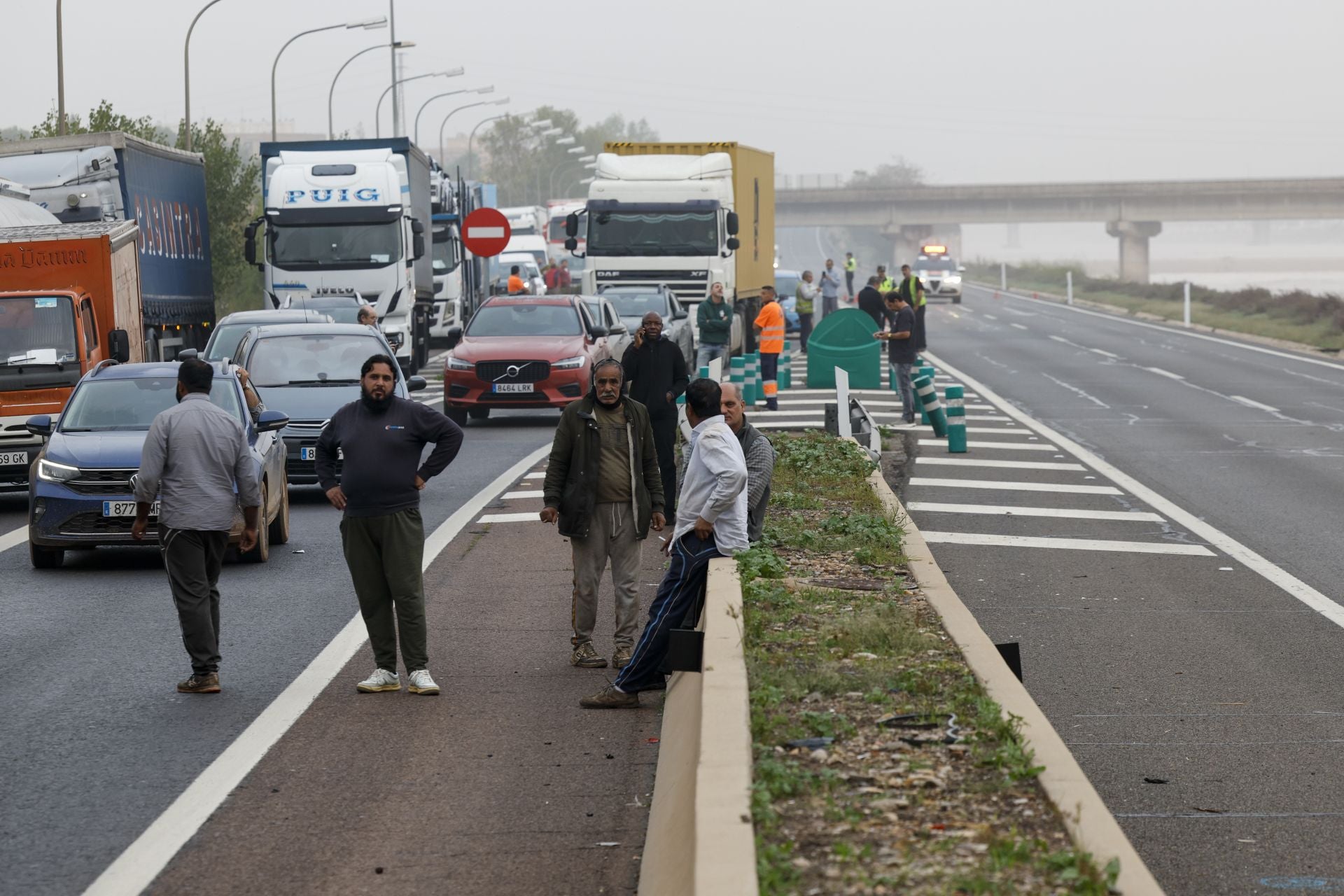 Varios conductores aguardan junto a sus vehículos en la V-30 junto al nuevo cauce del Turia durante la mañana de este miércoles en la que la red principal de carreteras de Valencia continúa cortada en varios puntos.