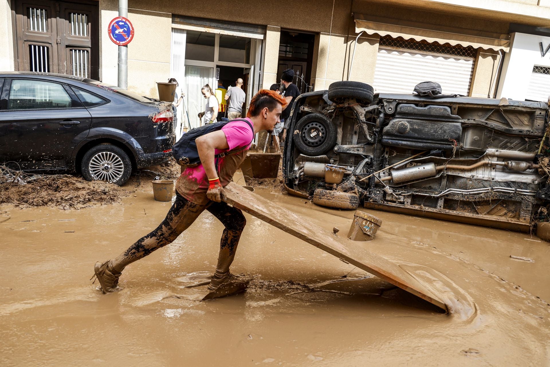 Una persona limpia barro con la ayuda de un tablón.