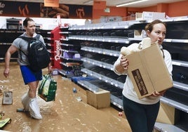 Dos personas recogen alimentos en un supermercado casi vacío de la localidad valenciana de Paiporta.