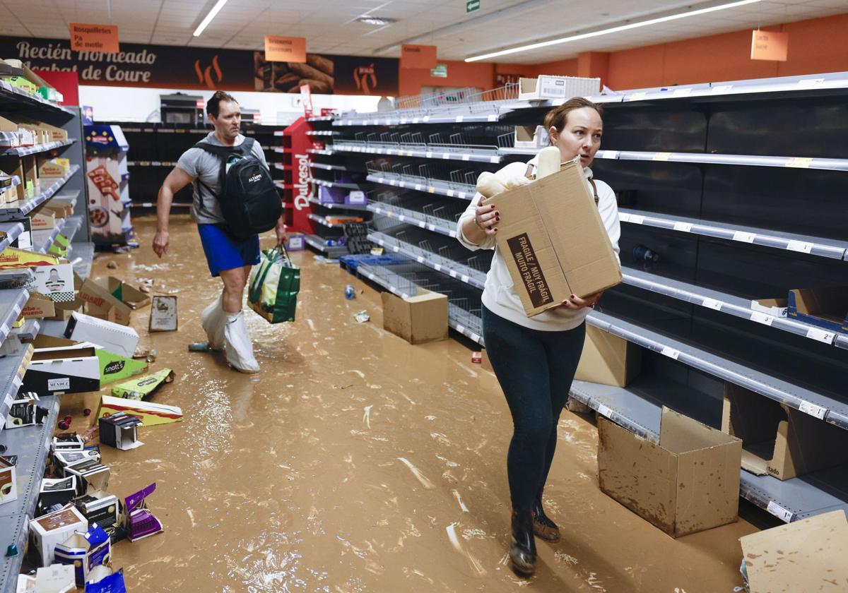 Dos personas recogen alimentos en un supermercado casi vacío de la localidad valenciana de Paiporta.