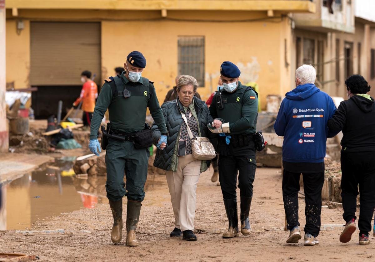 Agentes de la Guardia Civil ayudan a una mujer en Paiporta para desplazarse las calles embarradas.