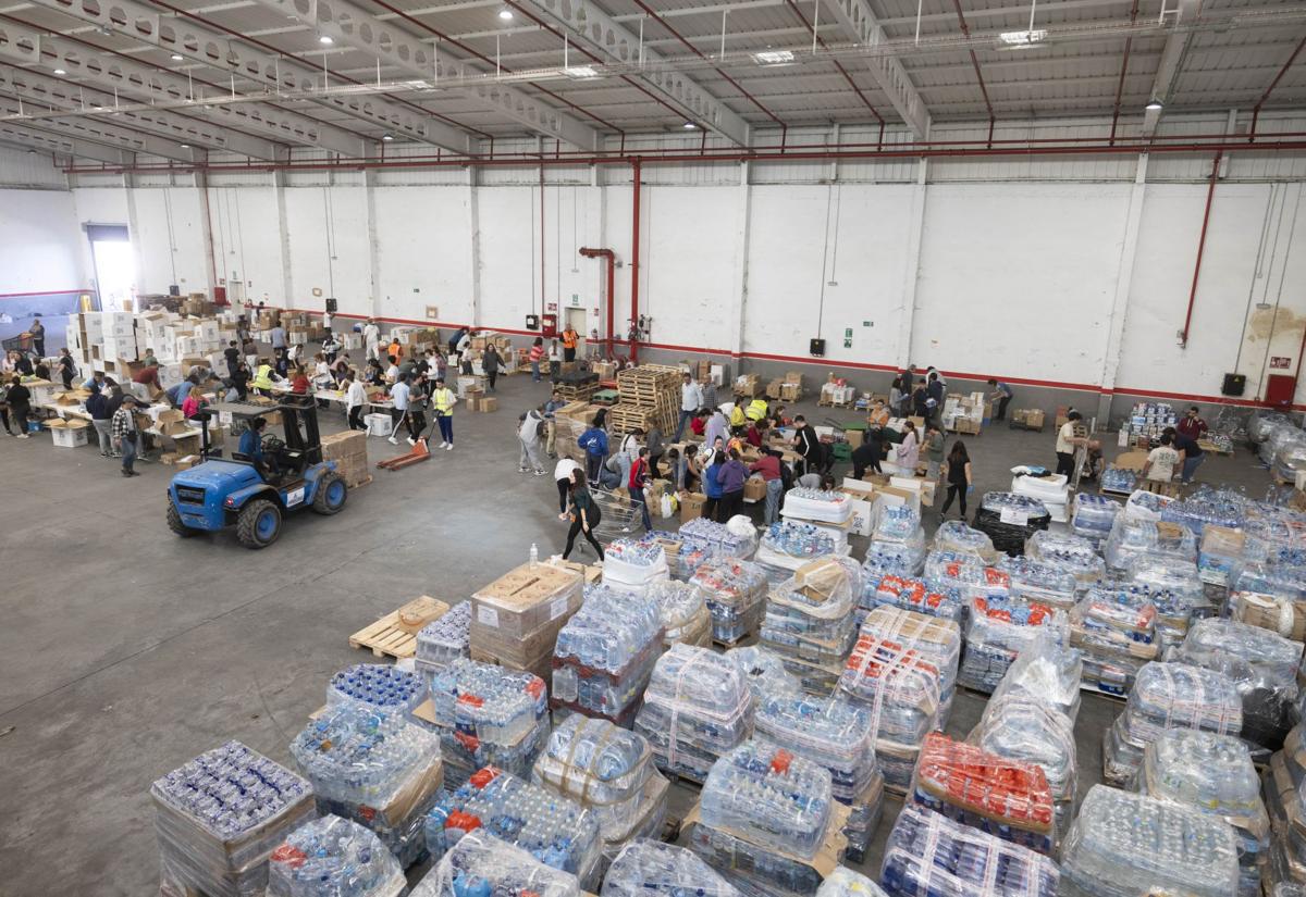 Imagen principal - Palés preparados para enviar a Valencia y voluntarios, este martes en la nave habilitada en el polígono de San Cristóbal.