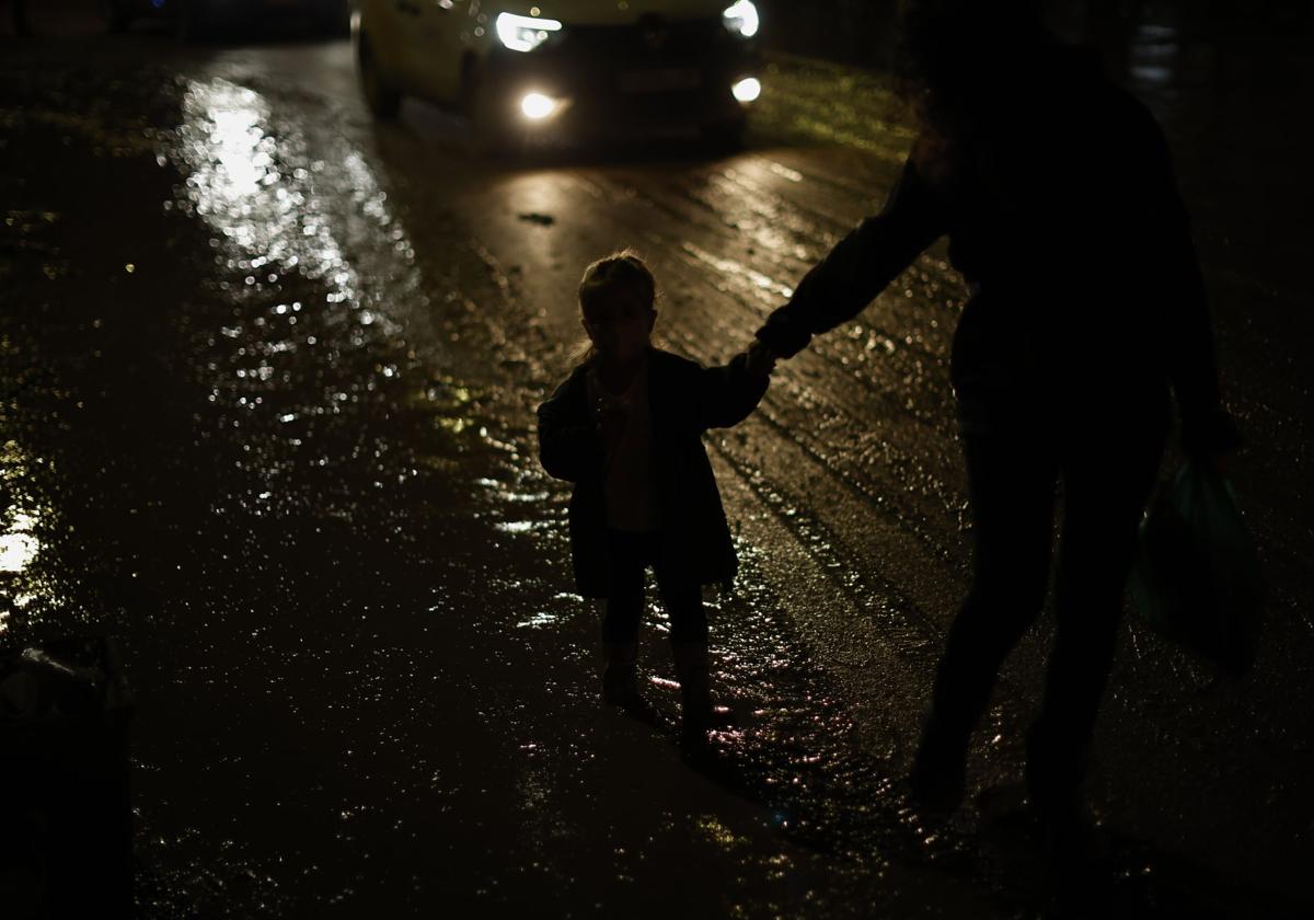 Un niño camina de la mano de un adulto por las calles de Paiporta, de noche, tras la Dana.