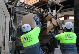 Dos trabajadores recogen cajas y residuos de la zona comercial de la Calle Mayor.