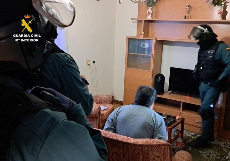 La Guardia Civil, en la operación, con uno de los detenidos en el salón de la casa.