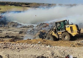 Una excavadora echa arena en los montones que arden en el vetedero de Martín Miguel.