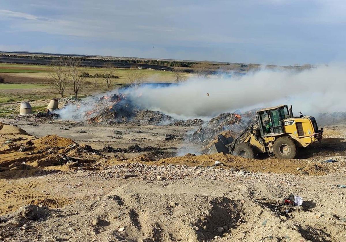 Una excavadora echa arena en los montones que arden en el vetedero de Martín Miguel.