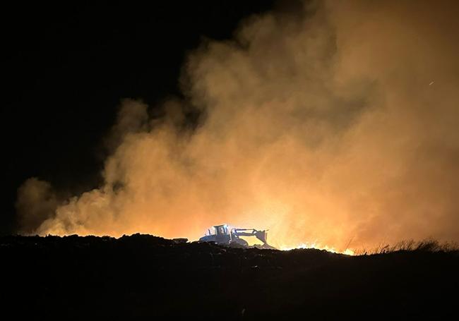 Una excavadora trabaja de noche en sofocar el incendio en el depósito de Martín Miguel.