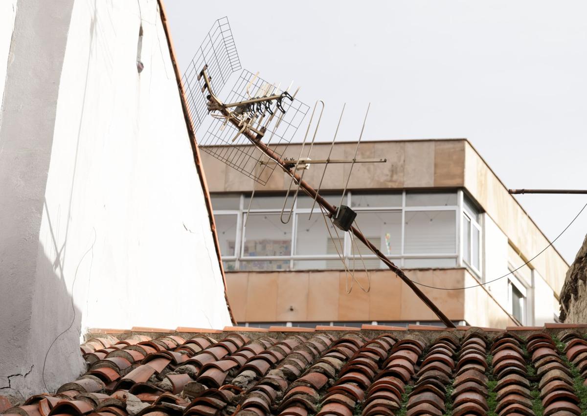 Imagen secundaria 1 - Una familia camina por el acceso peatonal junto al edifcio. La antena decolgada sobre el tejado y parte de la chimenea que se desprendió el 3 de noviembre.