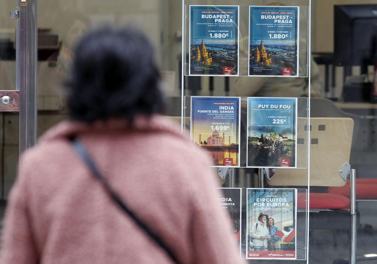 Una mujer observa varias ofertas de viajes en el escaparate de una agencia de la ciudad.