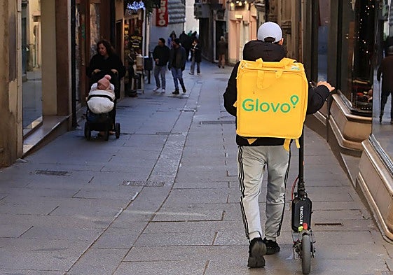 Un repartidor lleva el patinete de la mano por la Calle Real de Segovia, que es peatonal.