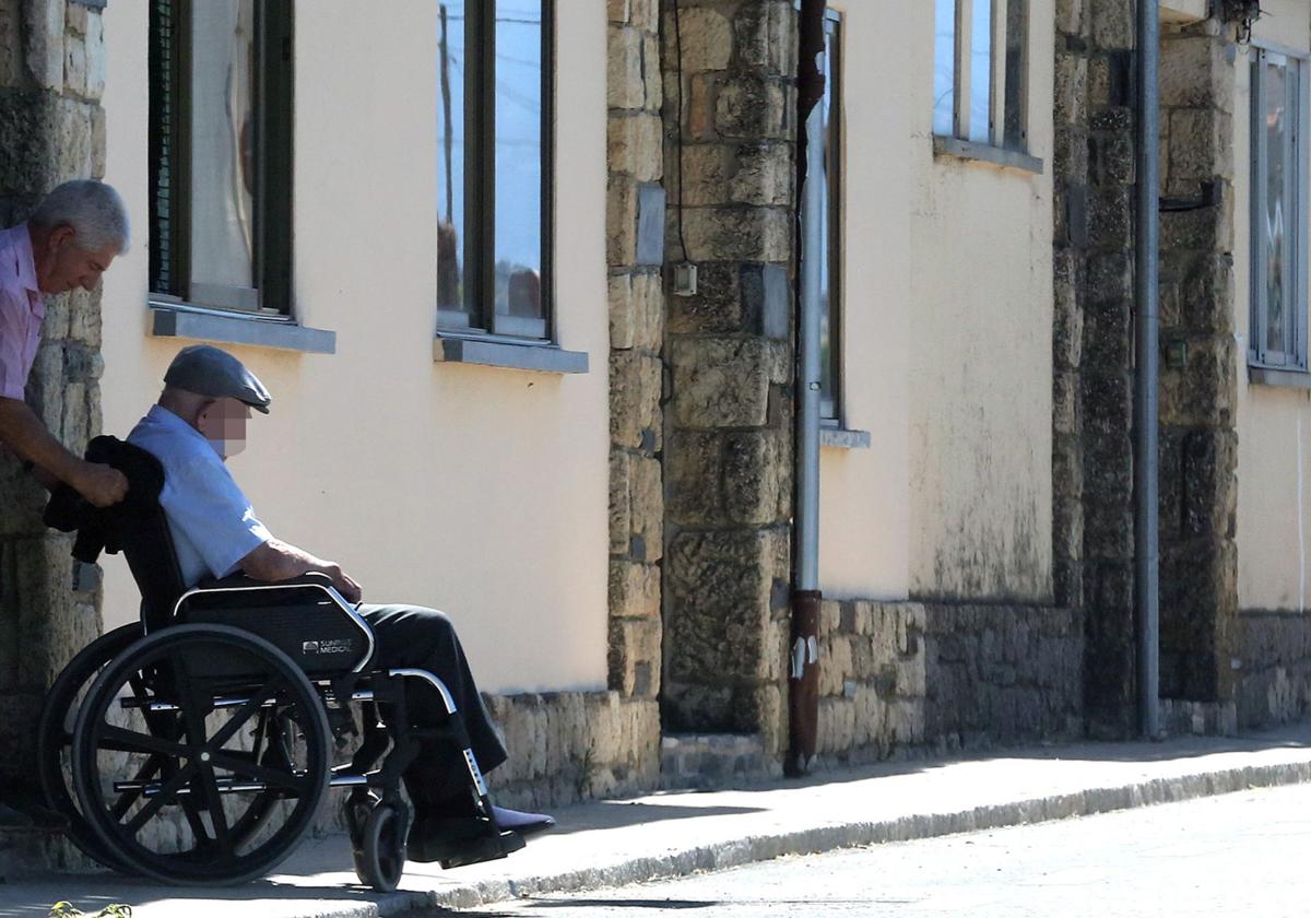 Un hombre saca a otro en silla de ruedas a la calle en un pueblo de Segovia.