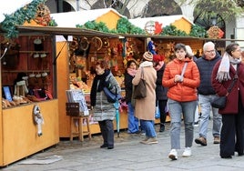 Segovianos y turistas pasean junto a los puestos del mercado navideño en la Plaza Mayor.