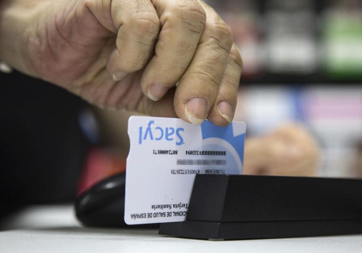 Un farmacéutico pasa la tarjeta sanitaria por la banda lectora.