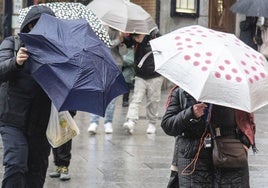 Viandantes por una céntrica calle de Segovia pelean con el paraguas por el viento y la lluvia.