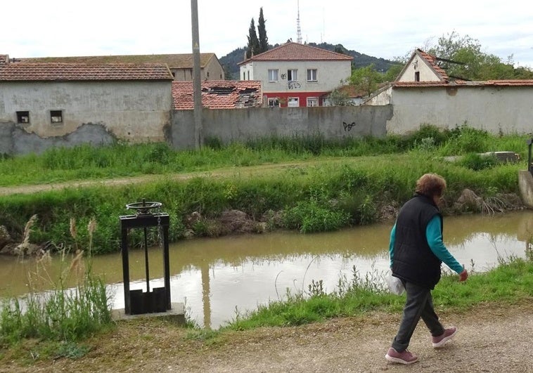 Una mujer pasea por el camino del Canal del Duero que discurre por el lateral de la Granja Luisa, en el polígono de San Cristóbal, donde se asoma la casa ocupada en el terreno municipal desde hace seis años.