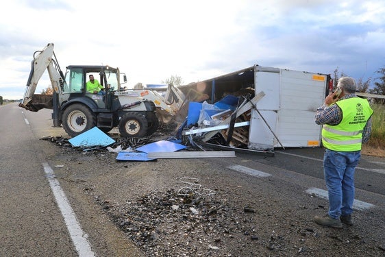Una excavadora retira la carga del camión volcado en la carretera.