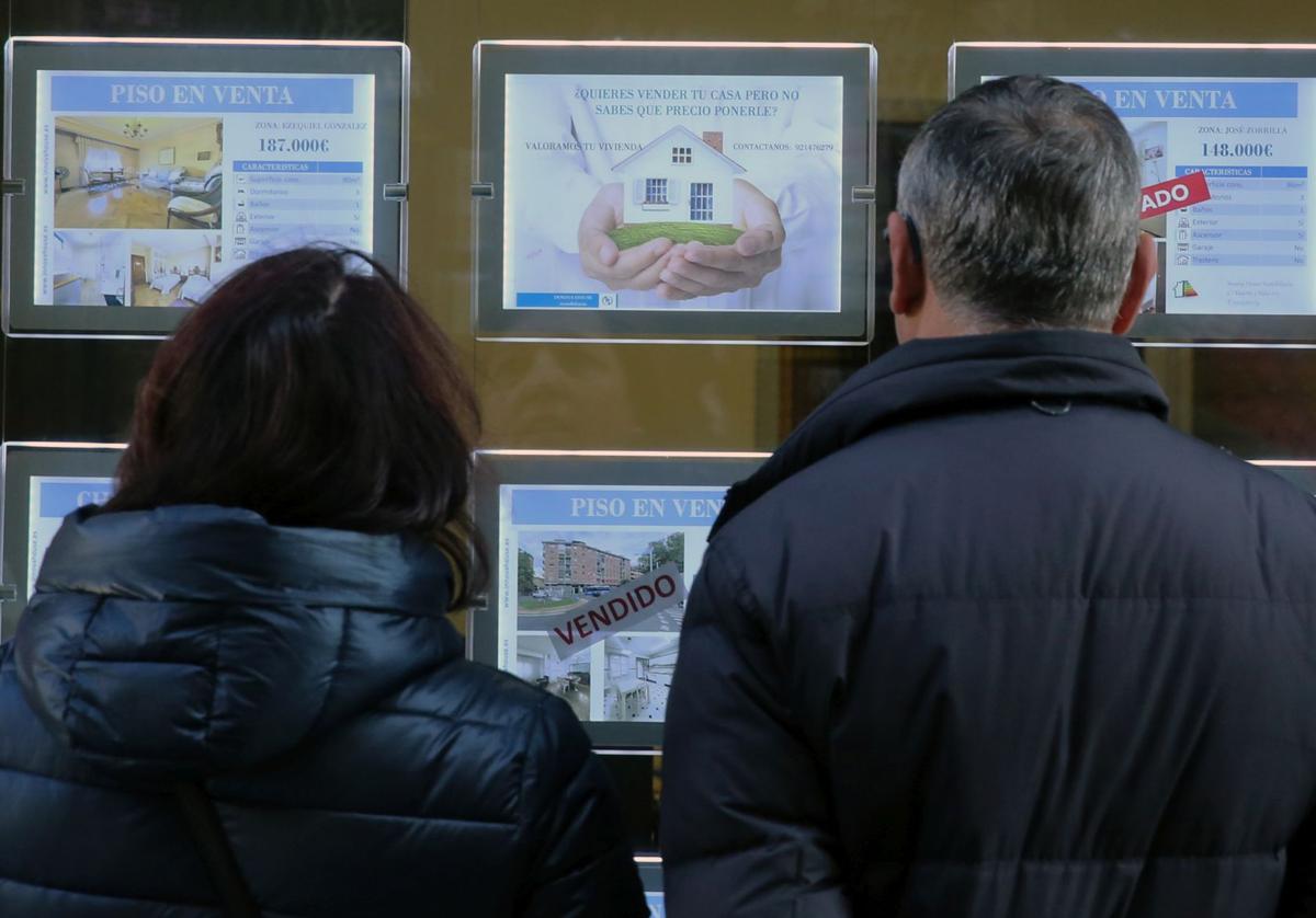 Una pareja observa ofertas de vivienda en el escaparate de una inmobiliaria de Segovia.