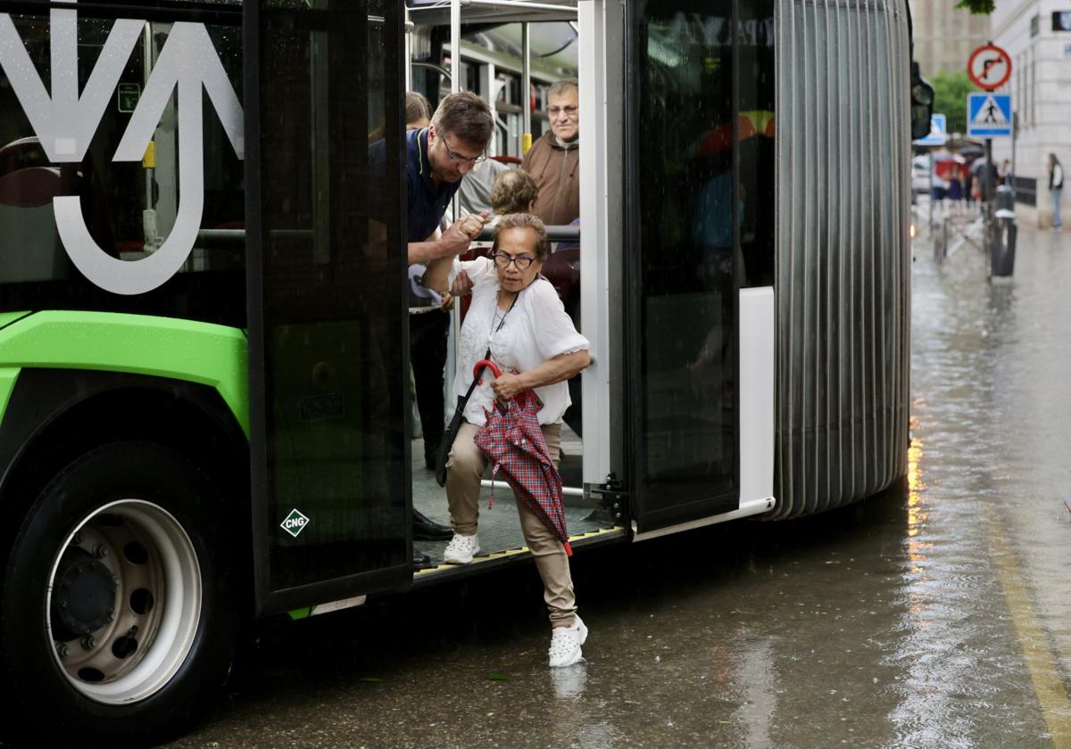 Un usuario ayuda a otra pasajera a bajar de un autobús urbano, el martes tras la tromba que inundó el centro.