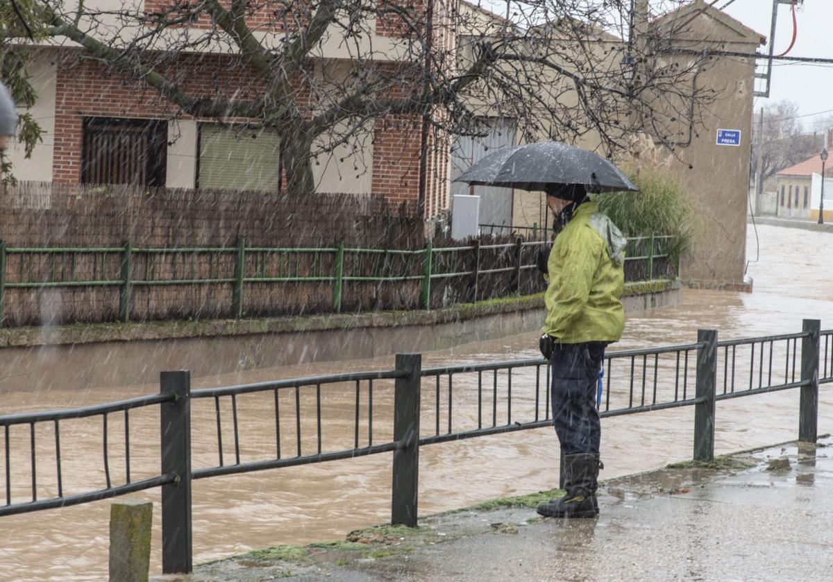 Un hombre junto a un arroyo crecido tras caer una troma de agua.