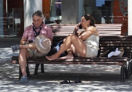Dos personas se refugian en la sombra de un banco.