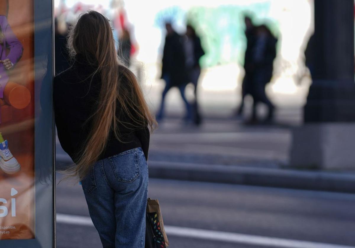 Una adolescente espera al autobús en una parada de transporte.