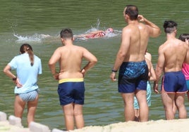 Un grupo de usuarios, al borde del agua en la playa de Las Moreras, mientras dos deportistas cruzan a nado ante ellos.
