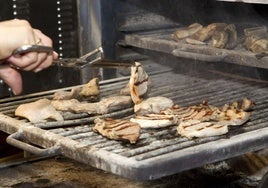 Una persona da la vuelta a la carne en una parrilla en una imagen de archivo.