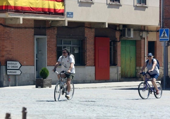 Dos personas pasean en bicicleta por un pueblo de Segovia durante los meses de verano.