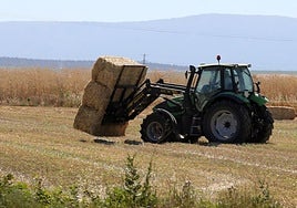 Un tractor deposita varias balas de paja en un campo cerca de Segovia.