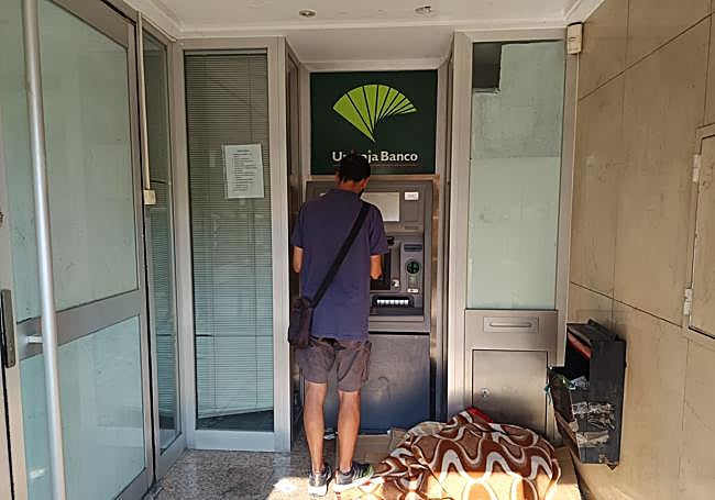 Un hombre saca dinero del cajero donde pernoctan las personas sin hogar.