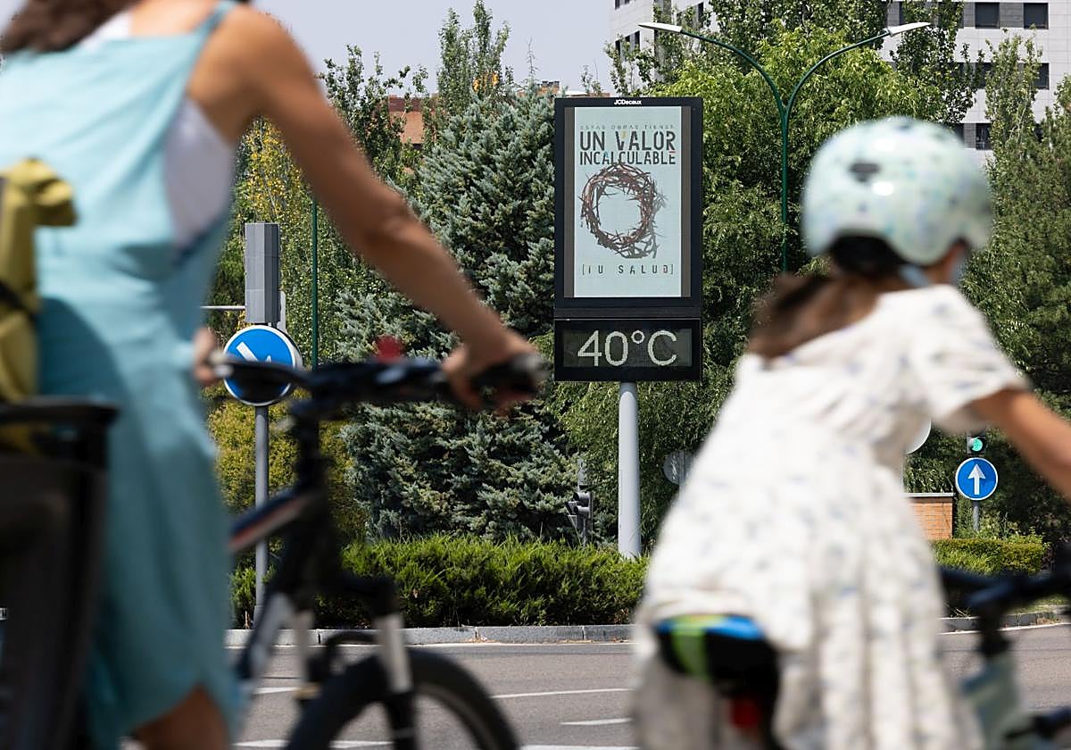 Dos ciclistas pedalean delante de un termómetro que marca 40 grados al sol en Valladolid durante esta ola de calor.