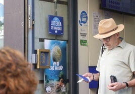 Un cliente sale de la administración de La Gorda, que tiene visibles los anuncios del sorteo de Navidad.