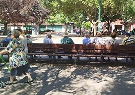 Varias personas mayores, sentadas en la plaza de los Vadillos.