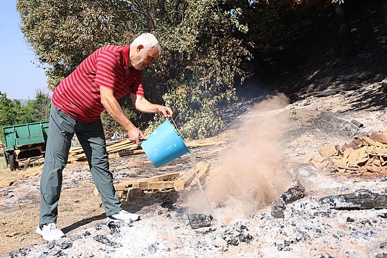 Un vecino de Palacios de Jamuz echa agua a un resquicio del fuego, que todavía ardía este viernes.