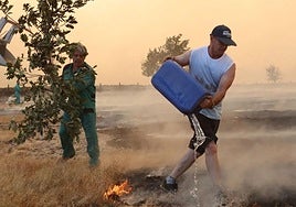 Dos personas se esfuerzan en apagar el fuego de Cipérez este viernes.