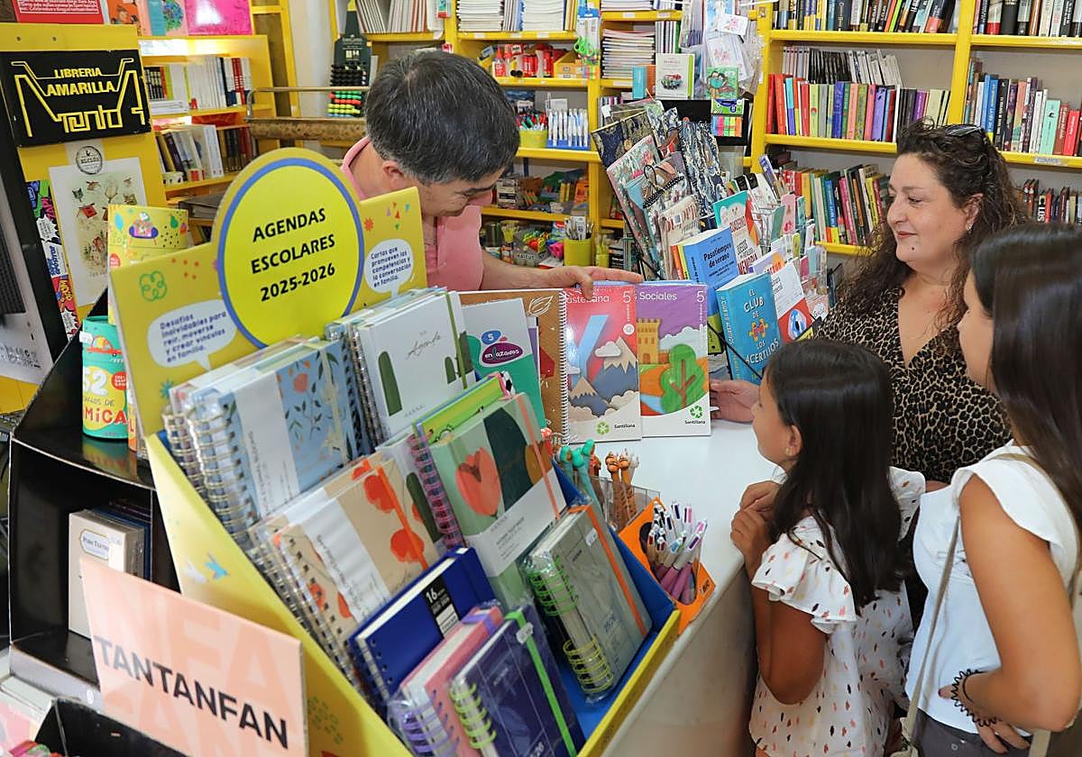 Juan Carlos Maté, de la Librería Amarilla, muestra unos libros de texto a una familia.