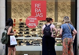 Viandantes se detienen a observar el escaparate de una zapatería de Valladolid que anuncia rebajas durante la campaña de verano.