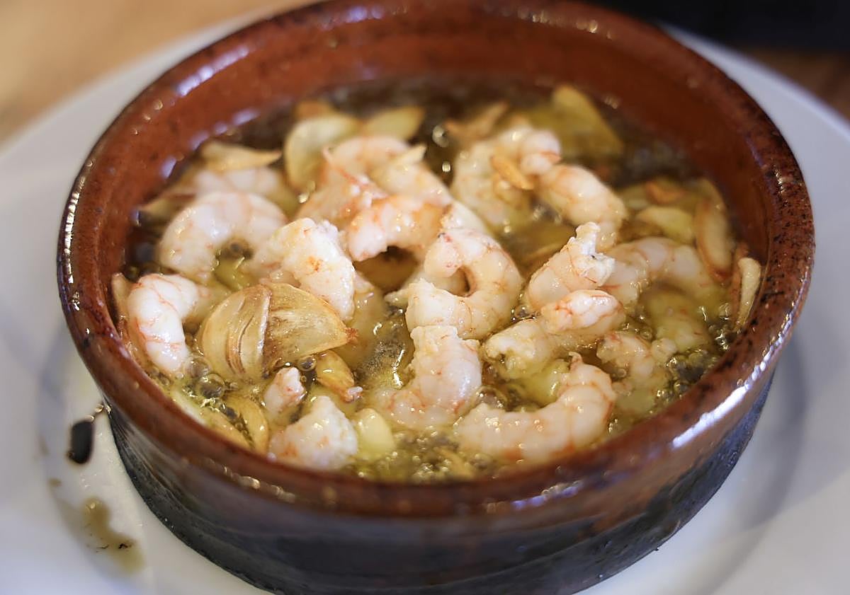 Imagen principal - Gambas al ajillo del restaurante El Pilar, terraza de El Concejo Hospedería y Restaurante, donde se celebran las 'Tardes de comedia' y estantería de vinos propios de Bodegas Concejo.
