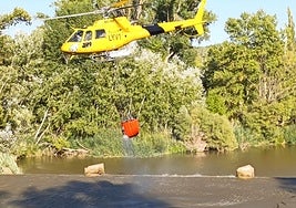 Un helicóptero carga agua en su cesta para sofocar un incendio registrado este domingo por la tarde en Tudela de Duero.
