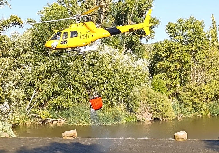 Un helicóptero carga agua en su cesta para sofocar un incendio registrado este domingo por la tarde en Tudela de Duero.