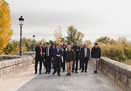 El consejero y el alcalde de Villamuriel, en primer término, pasean por el renovado puente sobre el río Carrión.