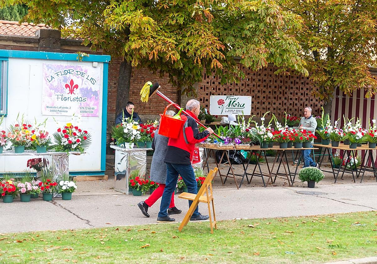 Un hombre lleva útiles de limpieza, a la entrada al cementerio, donde están instalados los puestos de venta de flores.