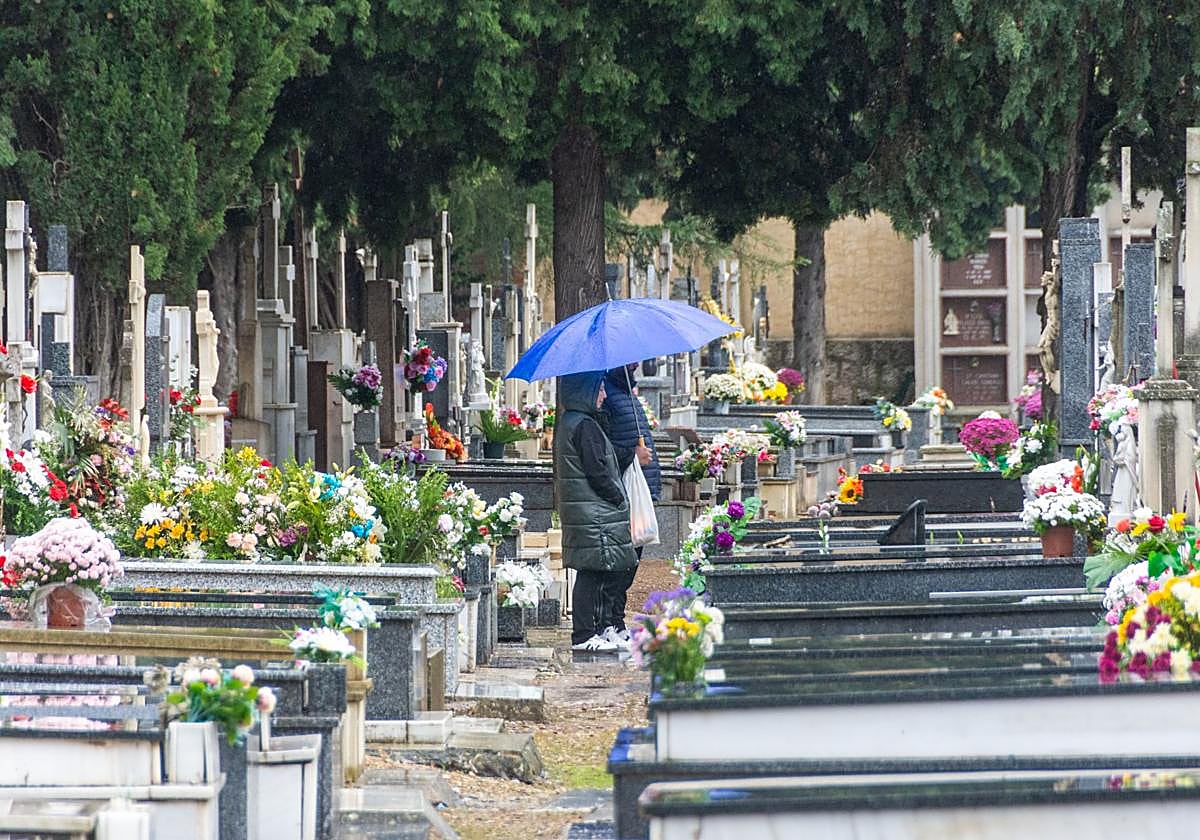 Dos personas se resguardan bajo un paraguas en el cementerio.