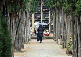 Dos mujeres caminan bajo la lluvia por una de las galerías del cementerio de Segovia.