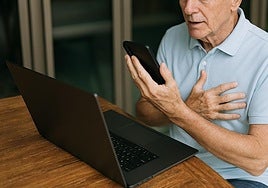 Una persona mayor utiliza el móvil y un ordenador portátil.