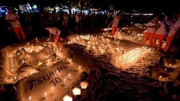 Varias personas encienden velas en la playa Patong. 