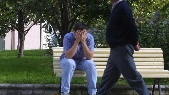Un hombre sentado en un banco se tapa la cara.