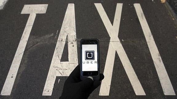 Un smartphone conectado a la aplicación Uber sobre el símbolo de taxis, en una calle de Madrid.